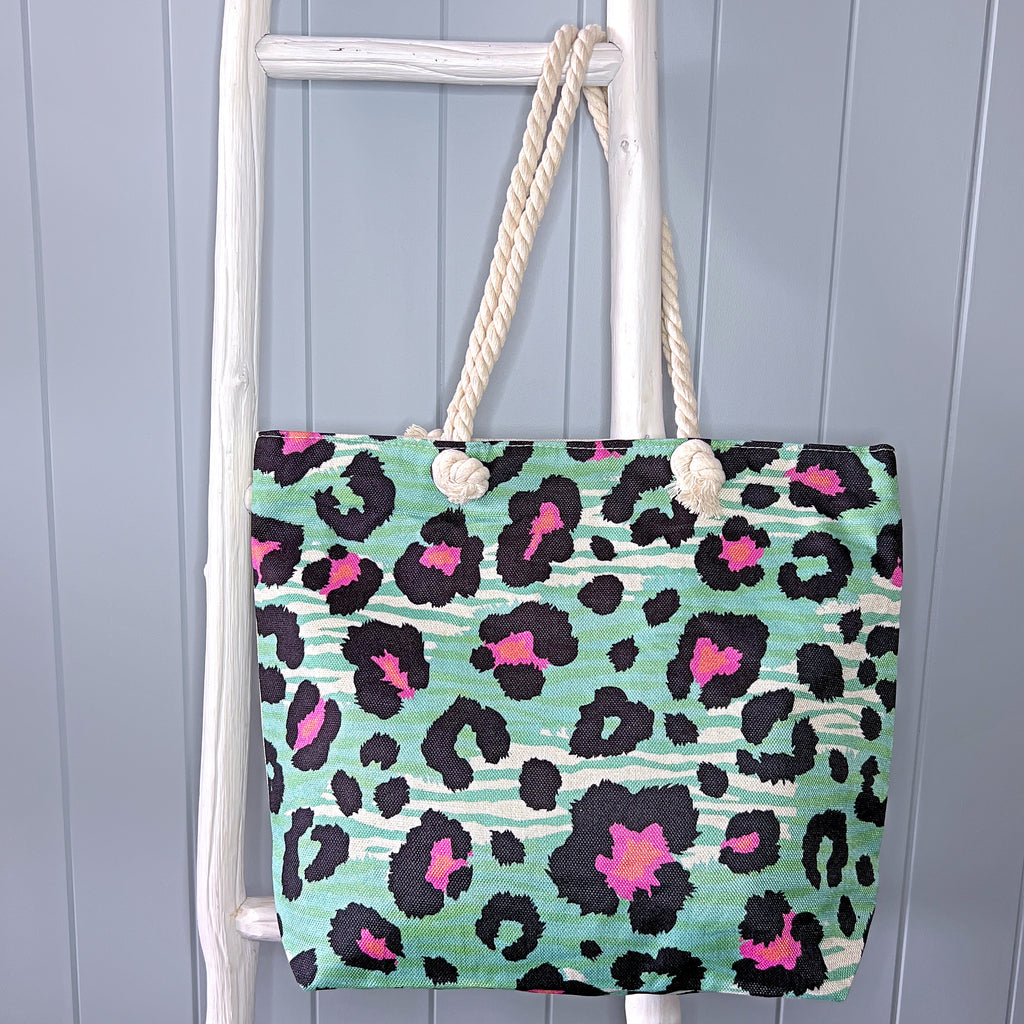 Personalised beach bag/beach tote hanging from a white timber ladder using it's rope handle. The bag has a pink and black animal print pattern over the top of a green animal-like stripe pattern.