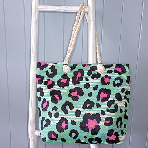 Personalised beach bag/beach tote hanging from a white timber ladder using it's rope handle. The bag has a pink and black animal print pattern over the top of a green animal-like stripe pattern.