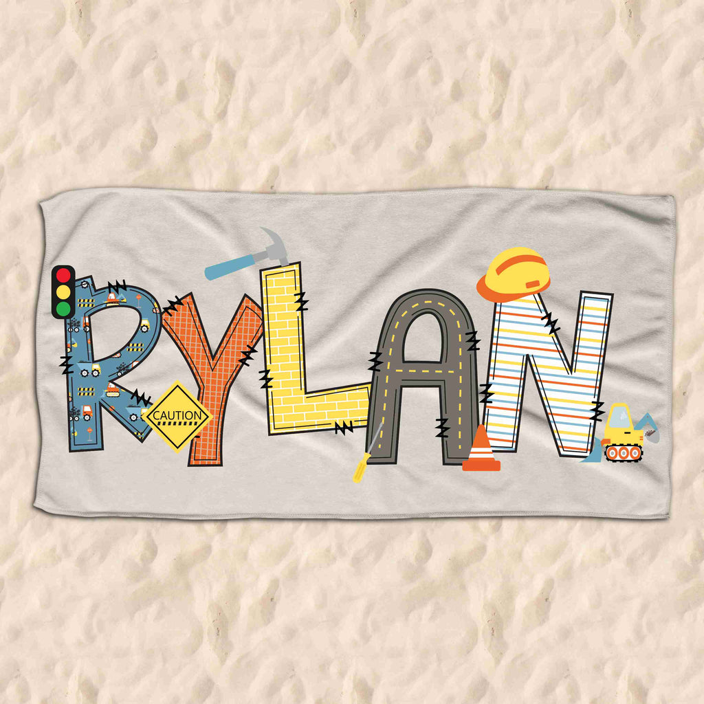 A children's size beach towel personalised with the name Rylan in block construction themed letters.