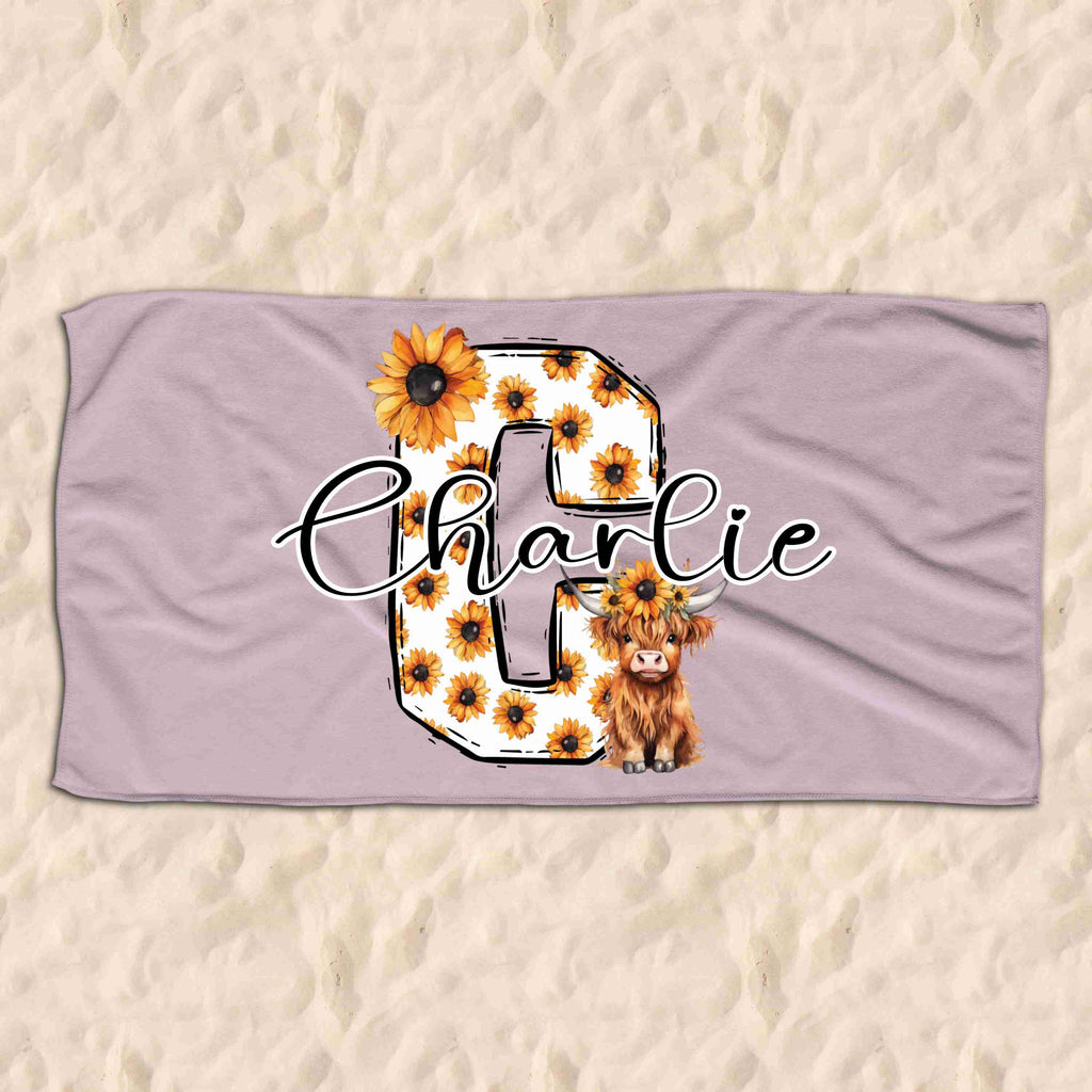 Beach towel with a large letter C monogram covered in sunflowers with a highland cow in the bottom right of the monogram. The name Charlie is then written across the C monogram in cursive font.