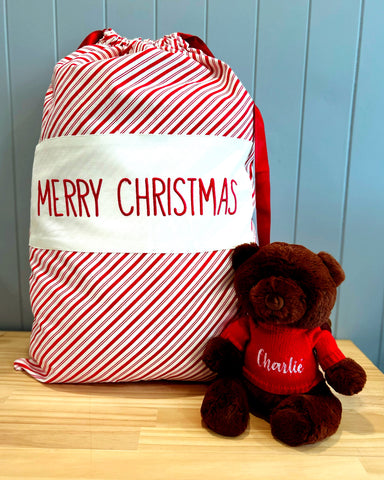 Large personalised Santa Sack with diagonal red and white stripes with a large natural coloured panel in the middle with the words Merry Christmas embroidered on it.