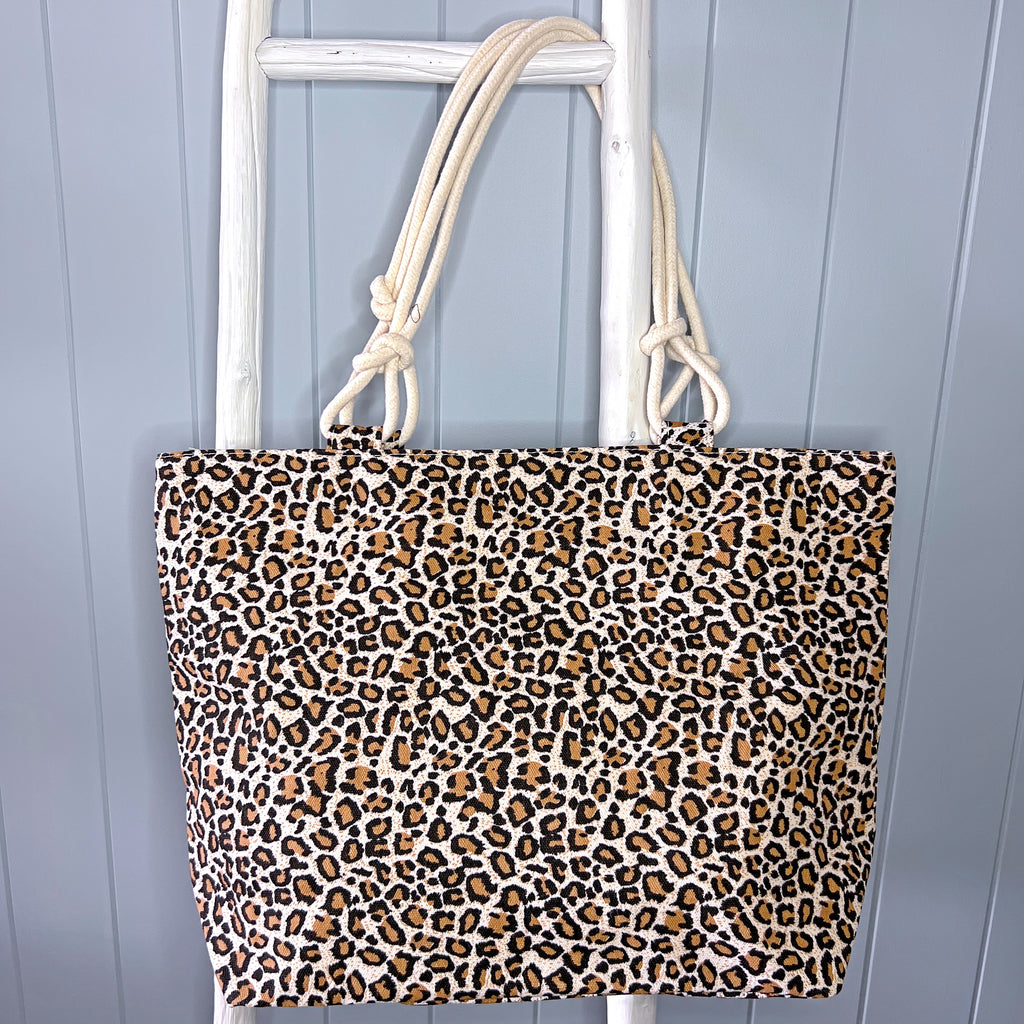 Personalised Beach Bag or Beach Tote Bag hanging from a white timber ladder from its rope handles. The bag is a small scale animal print in shades of brown and gold.