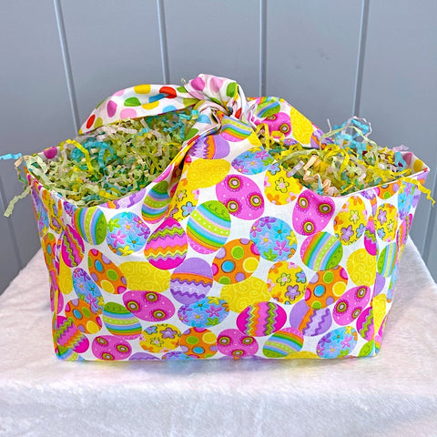 Handmade personalised easter basket bag with outer layer made out of colourful Easter egg fabric and inner lining in colourful spot fabric on a white background.