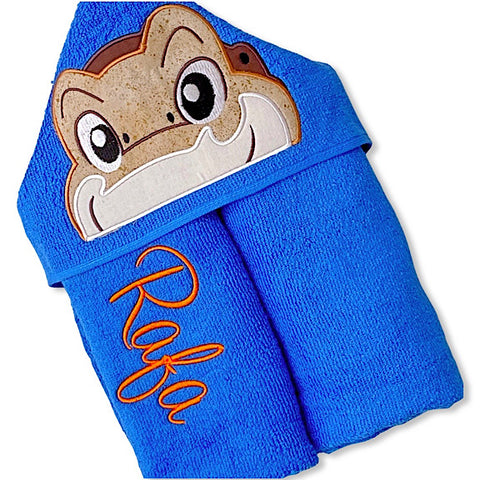 Hooded bath beach swim towel in blue with blue hood. Hood has a smiling dinosaur head appliquéd in the centre. Personalised with a name.