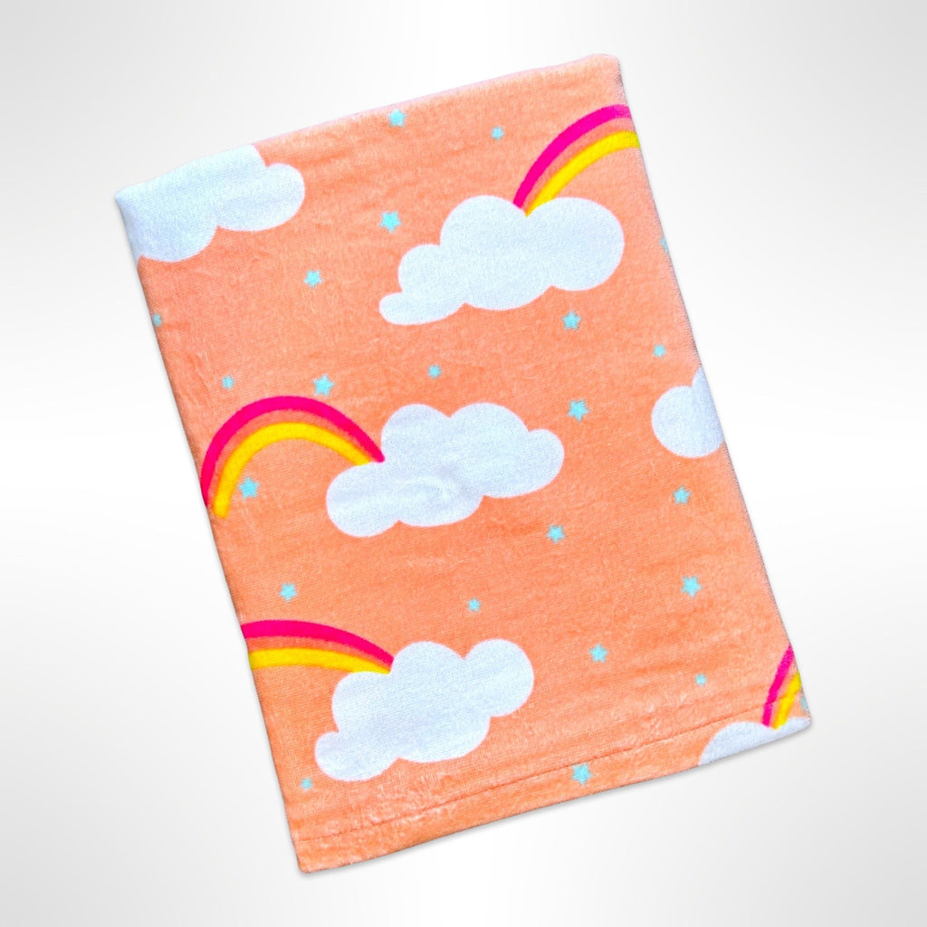 Children's personalised beach towel with rainbows and clouds on an apricot coloured background.