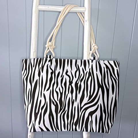 Personalised beach bag or tote bag hanging from a white timber ladder using its rope handle. The bag has a vertical black and white zebra stripe pattern.