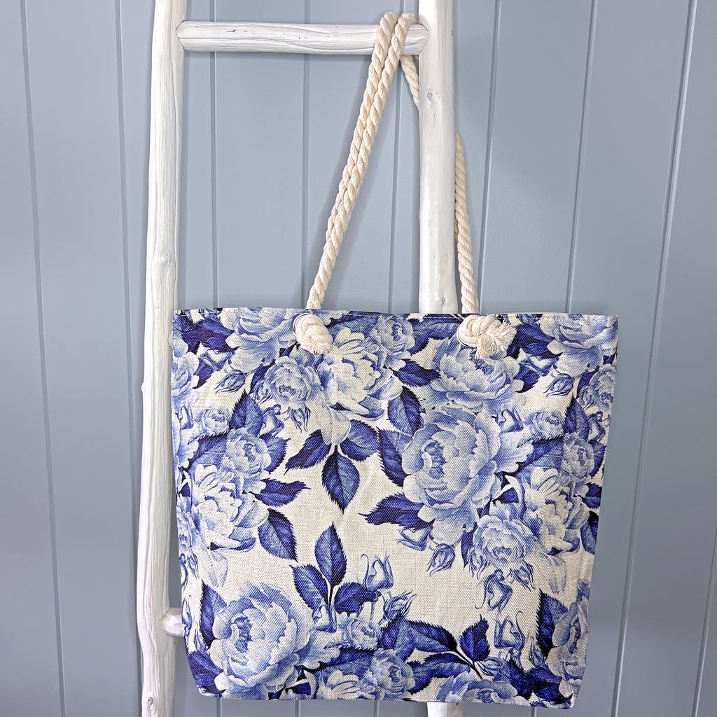 Personalised beach bag or beach tote hanging from a white ladder. The bag has a blue and white floral print similar to Hamptons style.