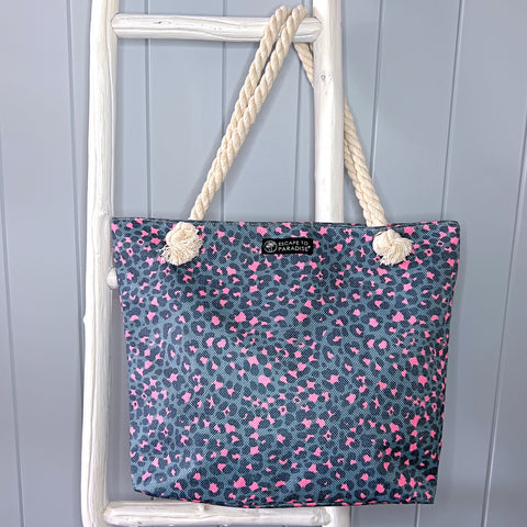 Personalised beach bag or beach tote hanging from a white timber ladder from its rope handle. The bag is a grey and pink animal print design.