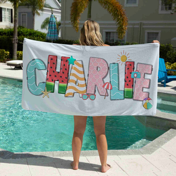 Beach towel personalised with the name Charlie being held up by a girl standing in front of a pool.