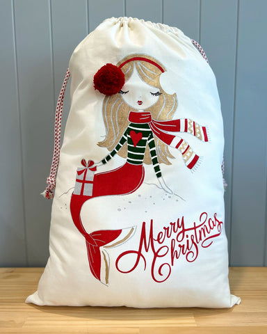 Large personalised Santa Sack with a picture of a gold haired mermaid wearing red and green holiday clothes with the words Merry Christmas in red underneath.