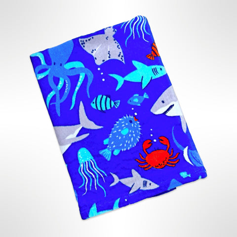 Childrens personalised beach towel that has sharks, crabs, octopus, fish and other sea life on a bright blue sea background.