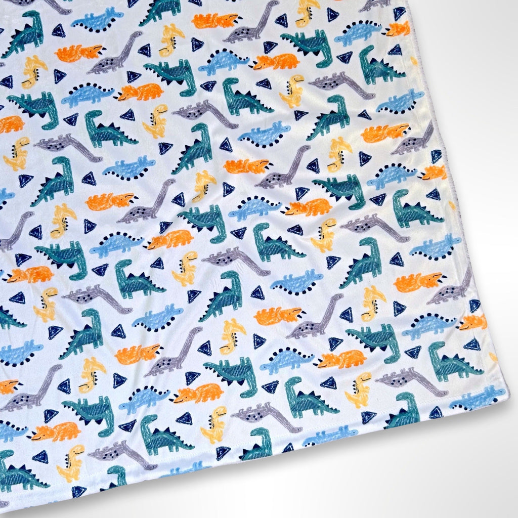 Minky fleece blanket with dinosaurs that look like they've been drawn with crayons in blue, orange and grey on a white background on one side and white fleece on the reverse, ready to be personalised with embroidery with a name