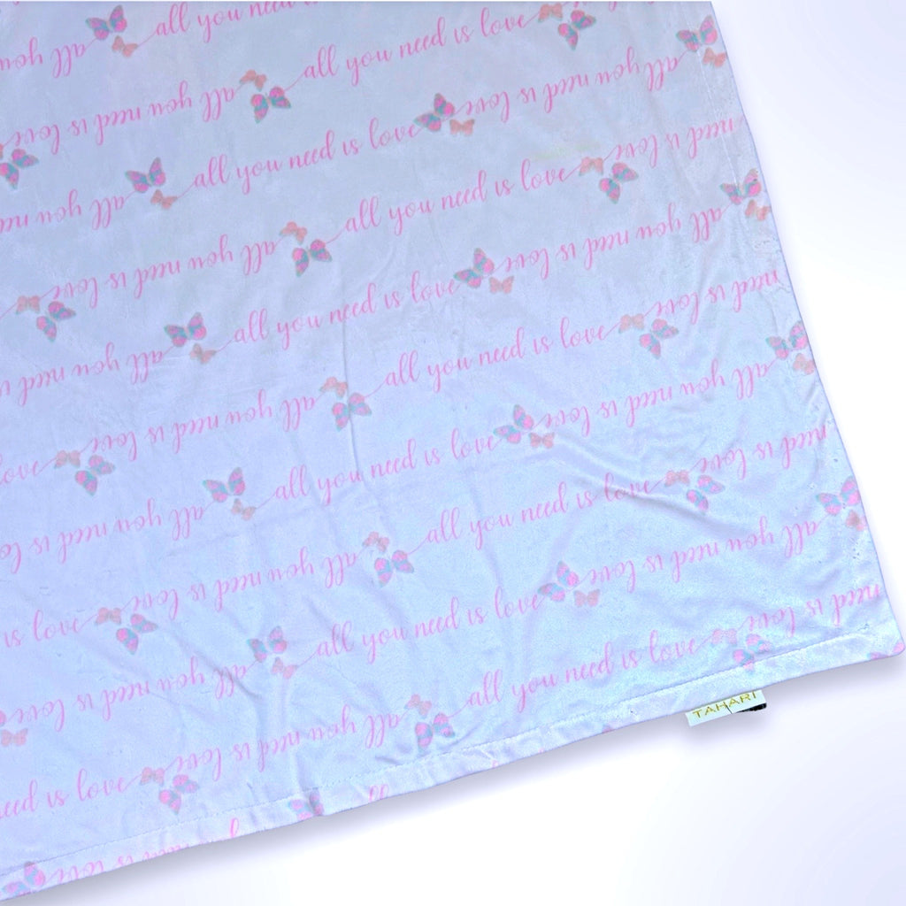 Double layer minky fleece blanket with the words all you need is love repeated in a pattern on a light pink background ready to be personalised with an embroidered name.
