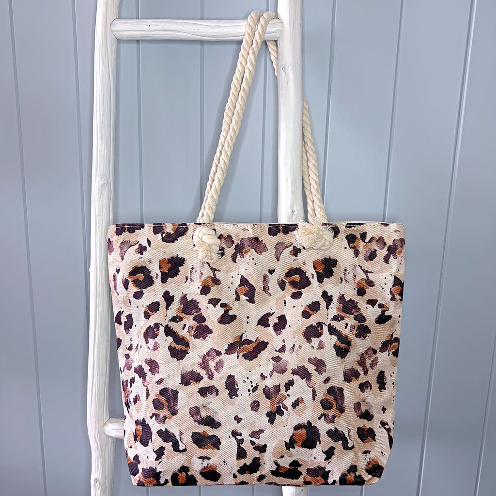 Personalised beach bag / beach tote hanging from a white wooden ladder. Bag has an animal print in shades of cream, beige, brown and gold. Bag is hanging from the ladder with it's rope handle.