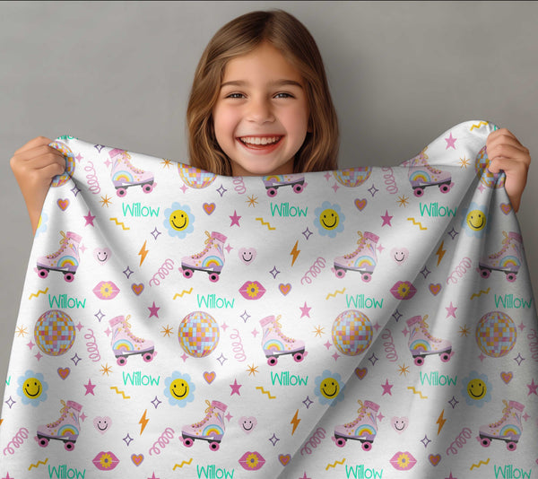 Smiling brown haired girl holding up a personalised minky blanket. The minky blanket has a mixture of roller-skates, disco balls, and other retro shapes along with the girl's name Willow.
