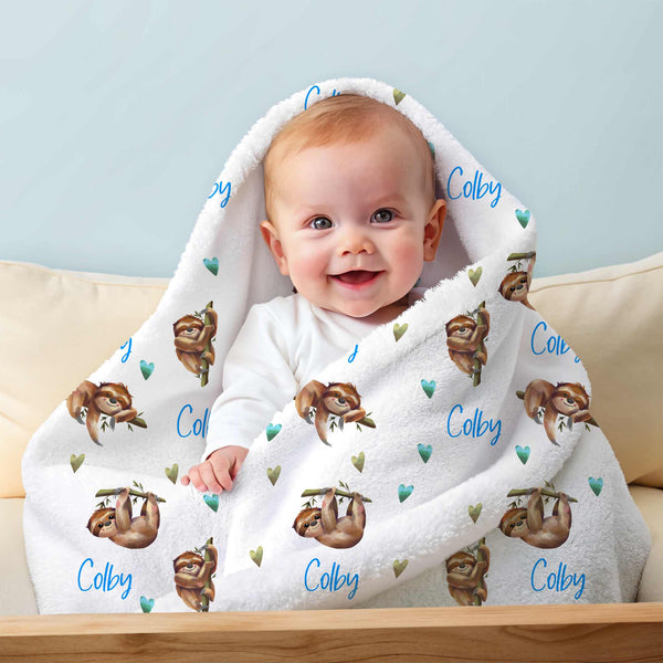 Smiling baby wrapped in a personalised minky blanket featuring brown sloths in various positions that has been personalised with the name Colby