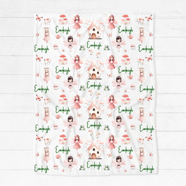 A personalised minky blanket lying on a white wooden floor. The blanket has various fairies among butterflies, mushrooms, frogs and flowers in pink shades, personalised with the name Everleigh.