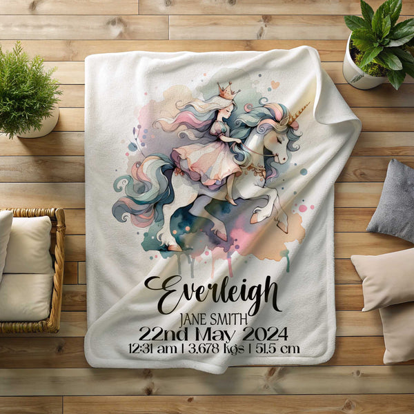 A white minky blanket lying on a timber floor surrounded by plants and cushions. The blanket has a picture of a princess riding a unicorn in pastel watercolour shades. The blanket is personalised with birth details including name, date of birth, time of birth, weight and length at birth.