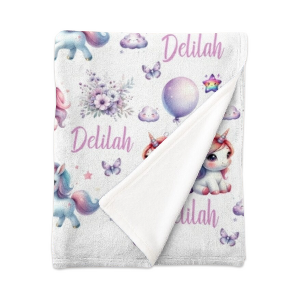 Folded white minky fleece blanket personalised with the name Delilah. The blanket has white unicorns with rainbow coloured manes among pastel coloured flowers, clouds, butterflies and stars.