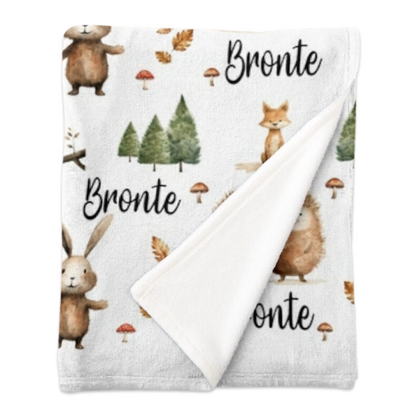 A folded personalised minky fleece blanket covered in woodland creatures in neutral shades.