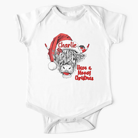 White short sleeved baby onesie bodysuit with face of black and white highland cow wearing a Christmas Santa Hat personalised with a name
