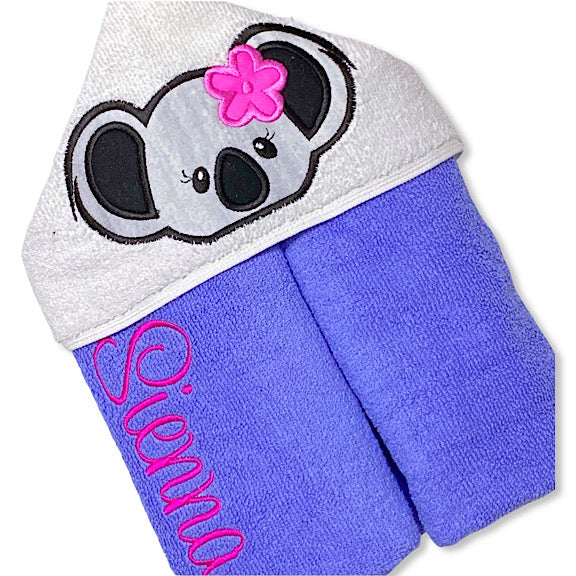 Hooded bath beach swim towel in purple with white hood. Hood has the face of a grey and black koala with pink flower behind ear appliquéd in the centre. Personalised with a name.
