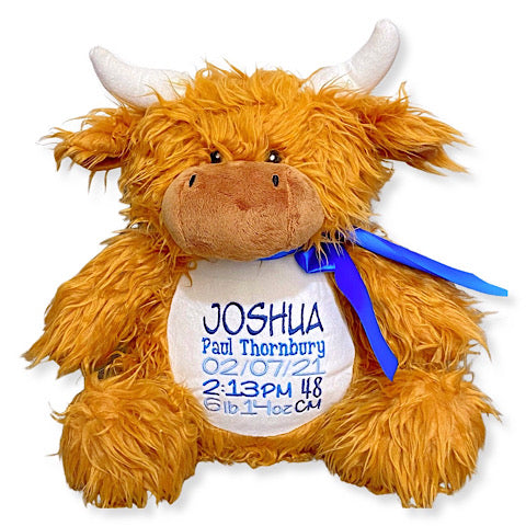 Shaggy brown highland cow plushie teddy with white horns personalised with baby birth details embroidered in shades of blue. A dark blue ribbon has been tied in a bow around the neck.