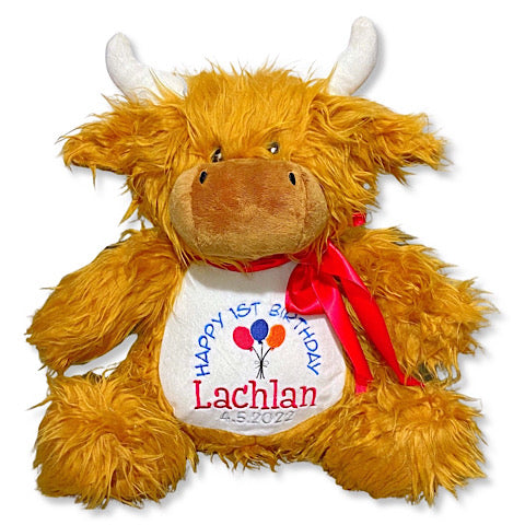 Shaggy brown highland cow plushie teddy with white horns personalised for a first birthday embroidered in blue, red and grey. A red ribbon has been tied in a bow around the neck.