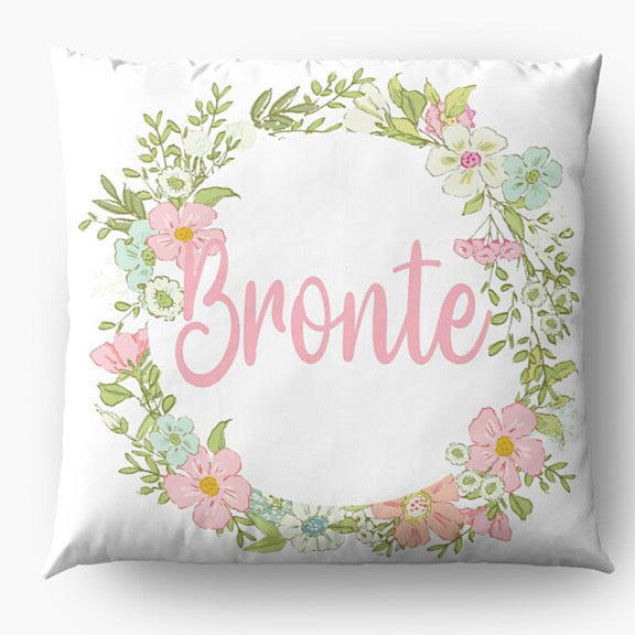 White cushion with a ring of pastel coloured flowers personalised with a name in light pink