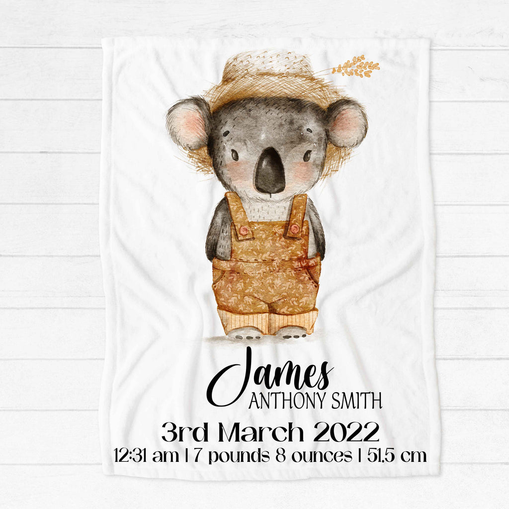 A white fleece minky blanket personalised with a name and birth details below a watercolour picture of a grey koala wearing a straw hat and brown coloured overalls like a farmer
