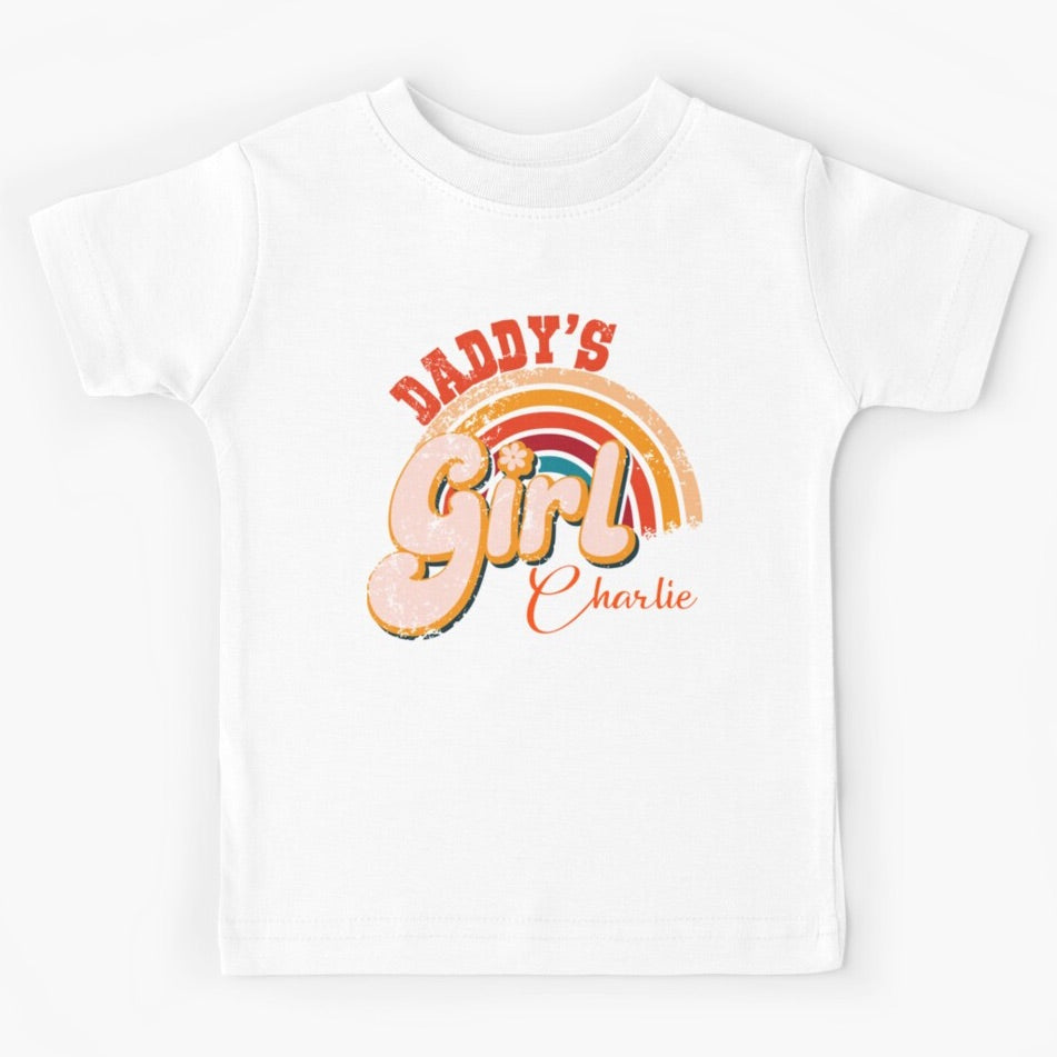 Short sleeved white kids t-shirt with Daddy's Girl written in retro 70s style writing over the top of a rainbow. The colours are a mix of reds, oranges and yellows. The shirt has been personalised with the daughter's name.