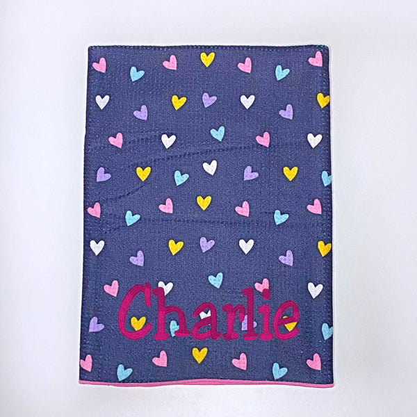 Beach towel with colourful hearts on a navy blue background personalised with a name.