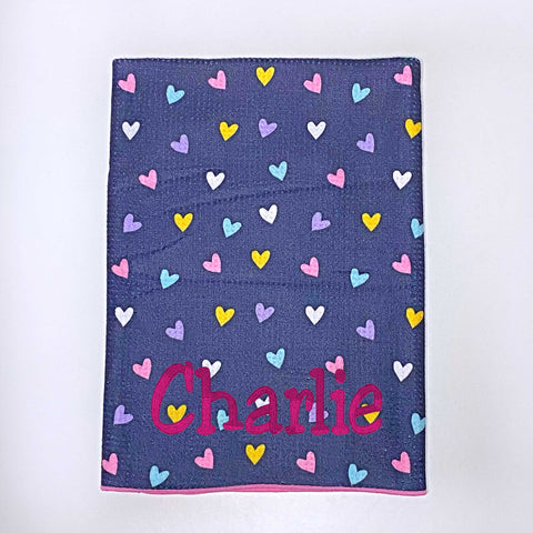 Beach towel with colourful hearts on a navy blue background personalised with a name.