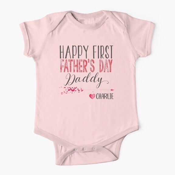 Light pink short sleeved baby onesie bodysuit with the words Happy First Father's Day Daddy in grey and red and personalised with the baby's name